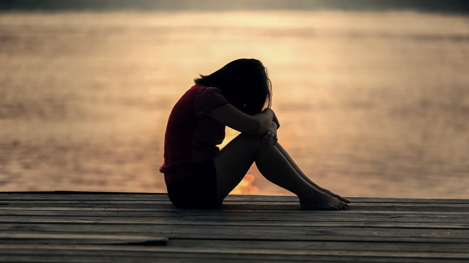 A girl sitting alone by the water at sunset, reflecting in silence.